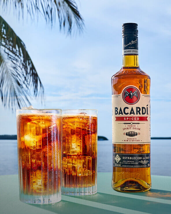 BACARDÍ Spiced rum bottle beside two tall glasses of rum and cola with ice.