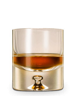 Short, heavy-bottomed glass filled with dark amber liquid, reflecting golden light.