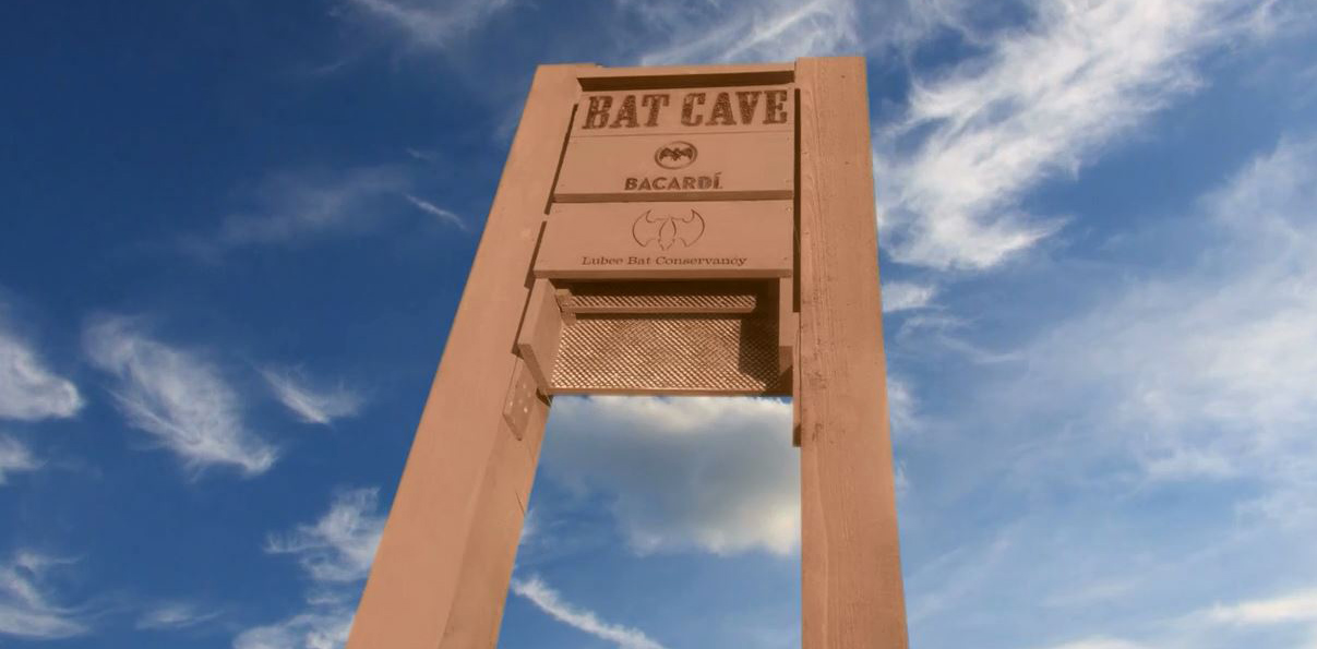 Large tan structure labeled "BAT CAVE" with BACARDÍ logo at Lubee Bat Conservancy entrance.