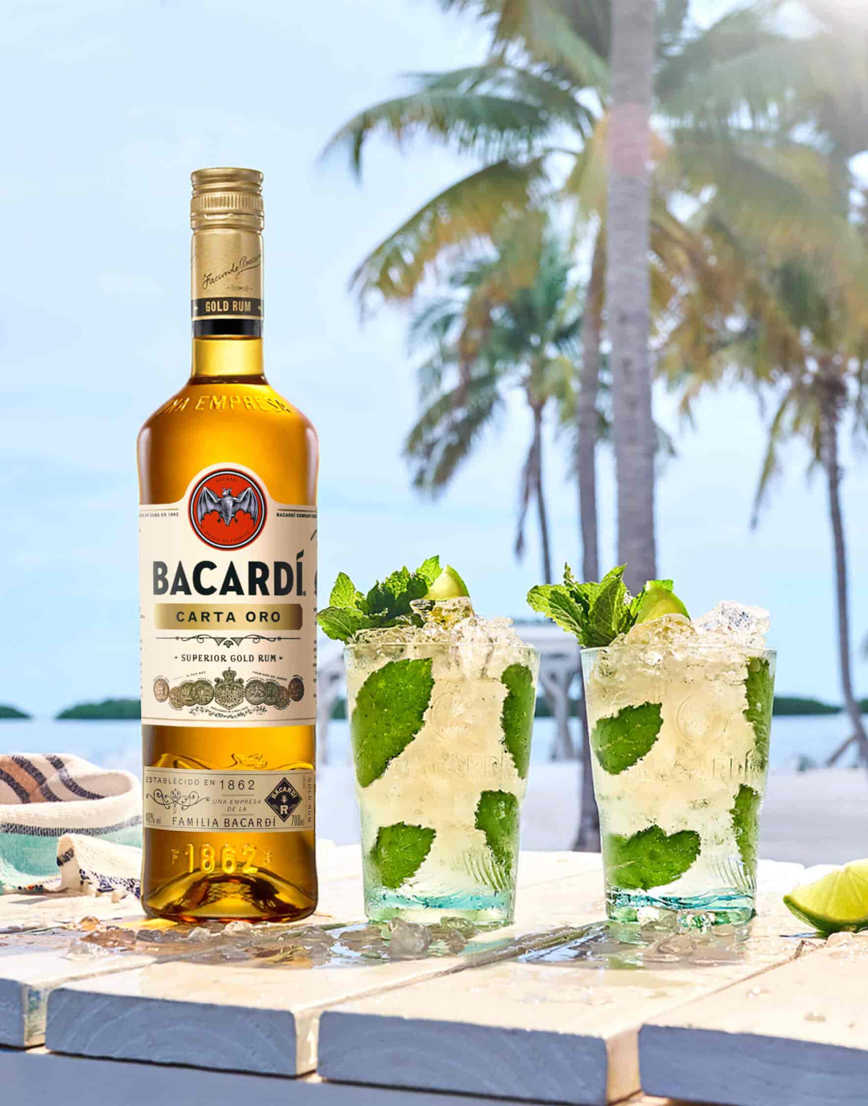 Bacardí Carta Oro rum bottle beside two mojito cocktails with mint and lime.