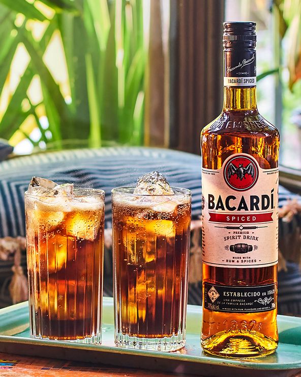 BACARDÍ Spiced rum bottle beside two tall glasses with dark iced cocktails.