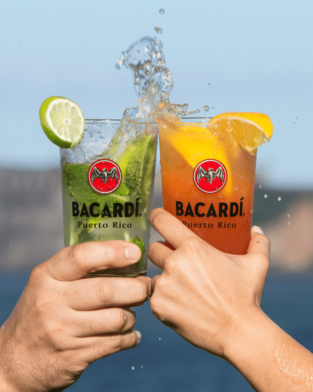 Two hands clinking Bacardí cocktails, creating a dynamic liquid splash.