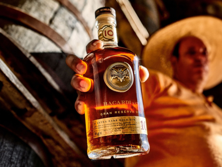 Hand holding BACARDÍ Gran Reserva Diez rum bottle with golden label.