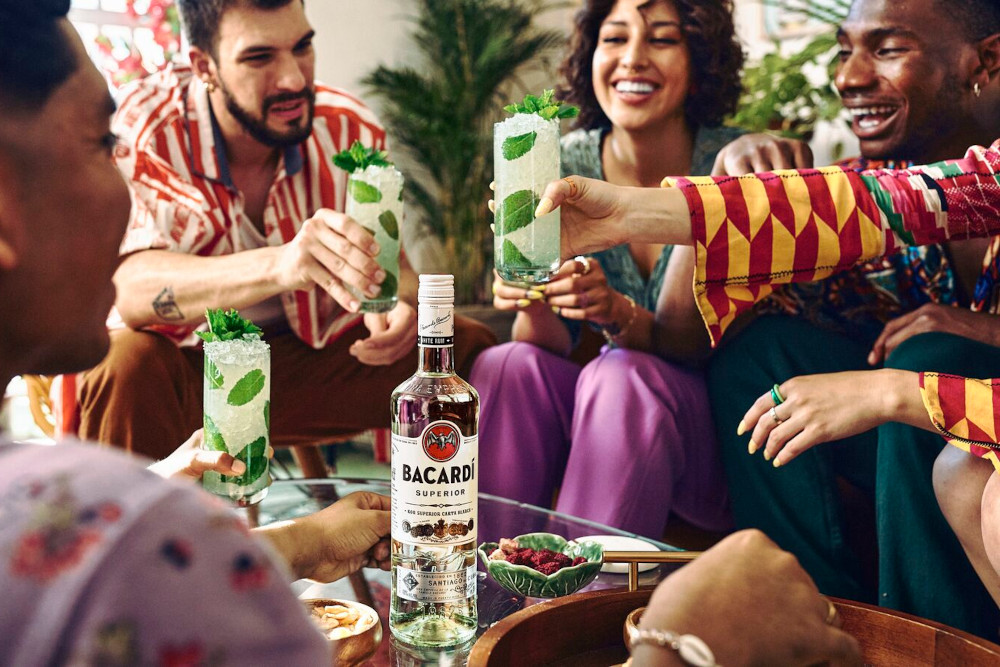 Group gathered around table with BACARDÍ rum bottle and mojito-style cocktails.