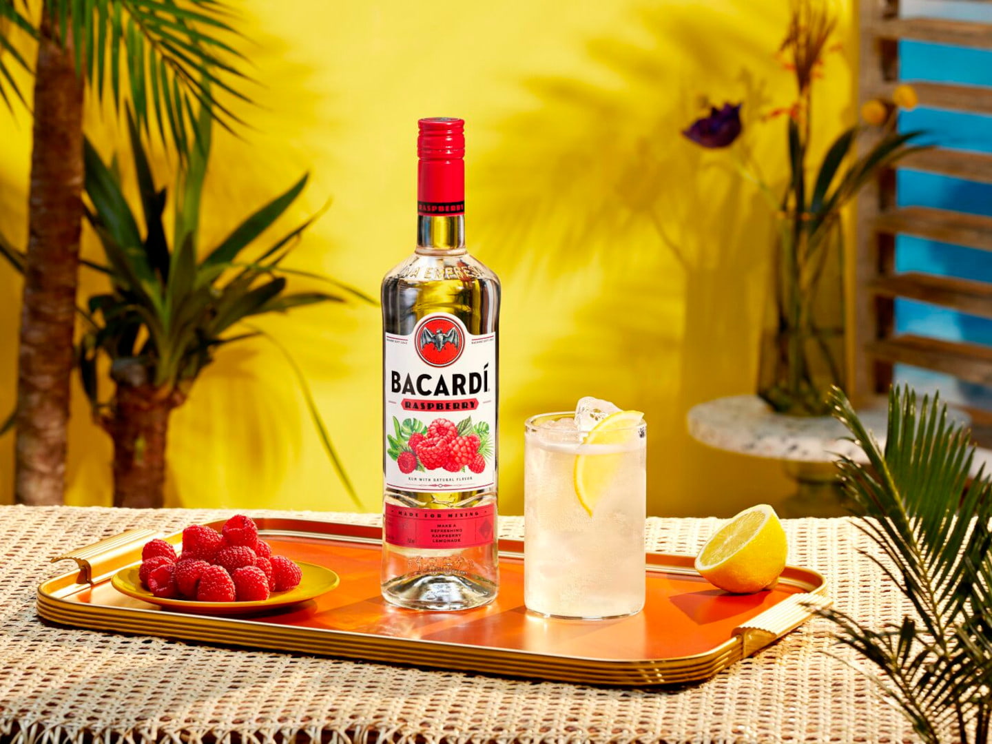 BACARDÍ Raspberry rum bottle with cocktail glass, fresh raspberries, lemon slice arranged on a tray.