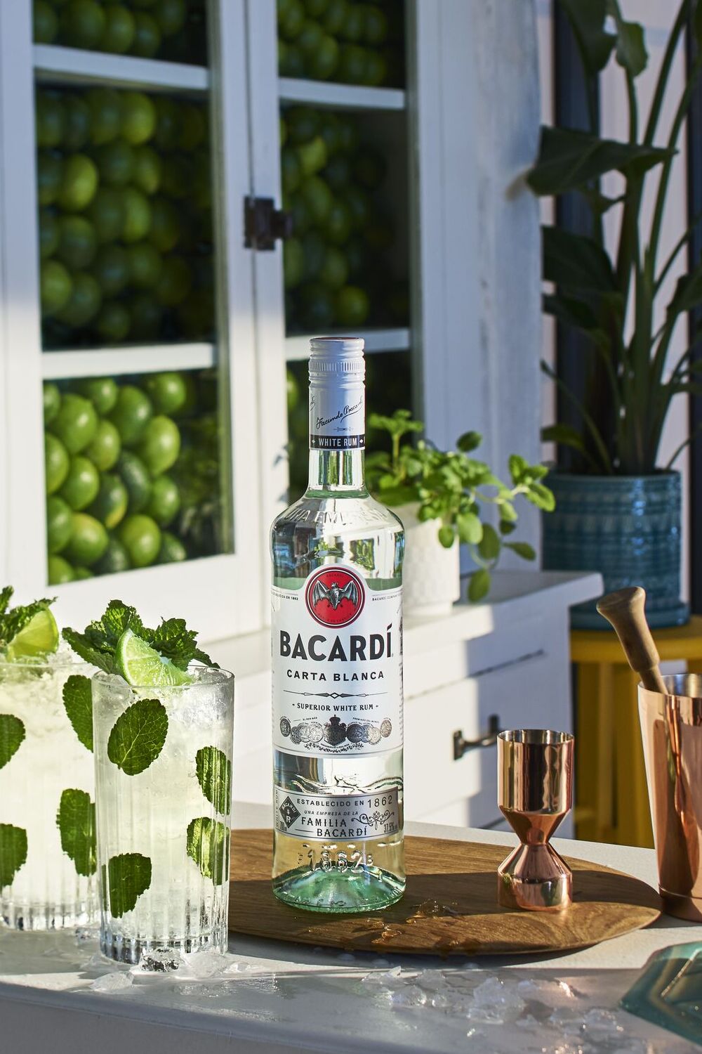 BACARDÍ Carta Blanca rum bottle with two mojito cocktails, lime wedges, mint leaves.