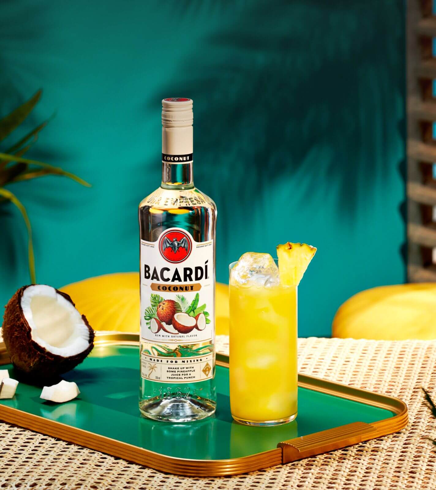 BACARDÍ Coconut rum bottle with yellow cocktail, pineapple wedge, halved coconut.