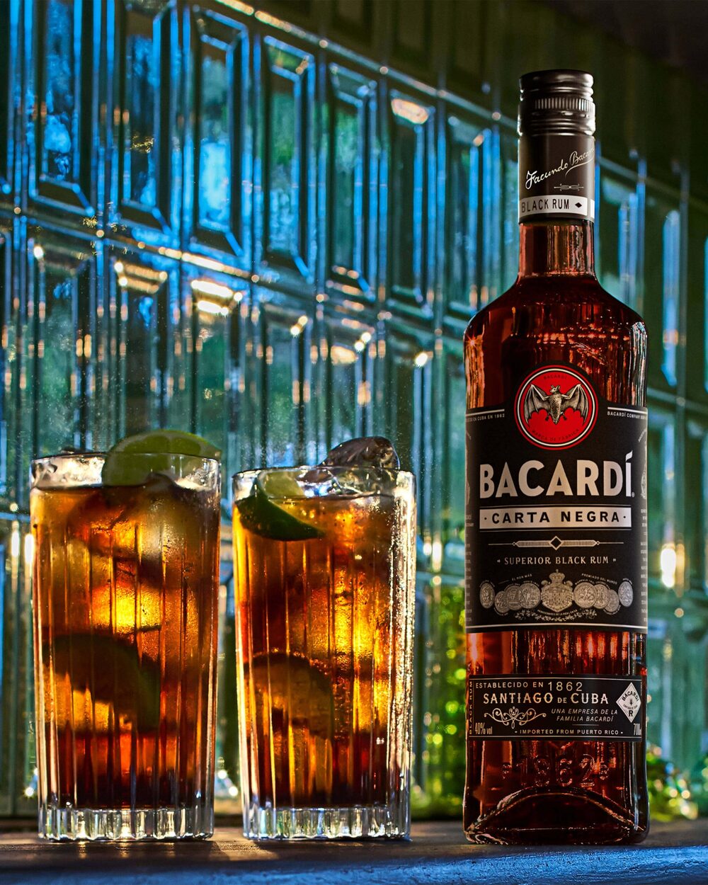 BACARDÍ Carta Negra black rum bottle with two tall dark cocktail glasses, lime wedges.