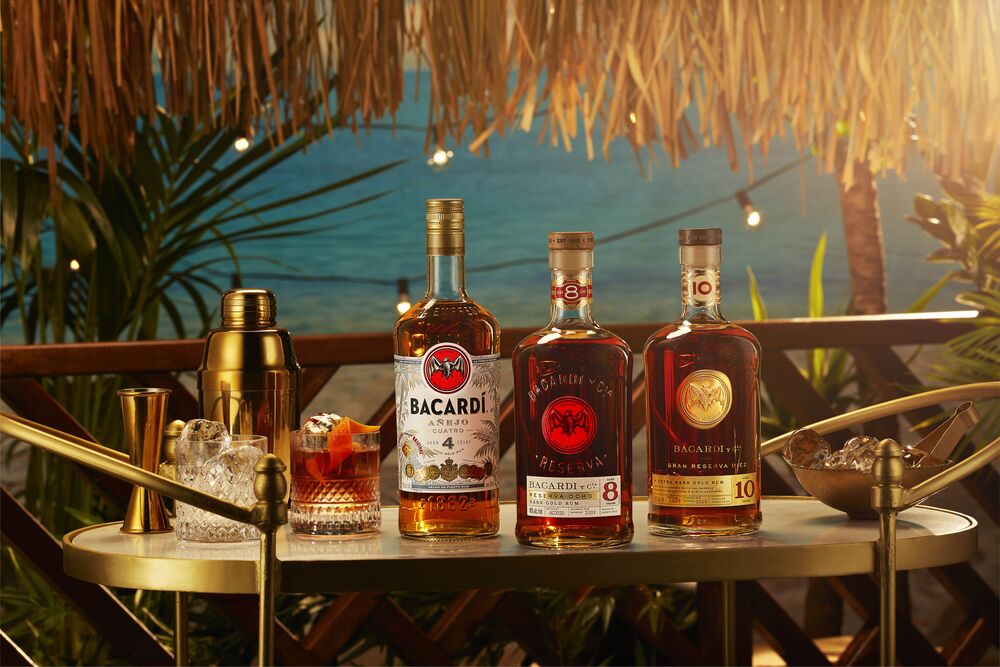 Three BACARDÍ rum bottles on a gold and white bar cart with cocktail accessories.