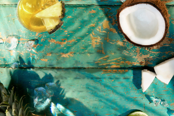 Overhead view of a cocktail with pineapple slice, split coconut, and scattered ice cubes.