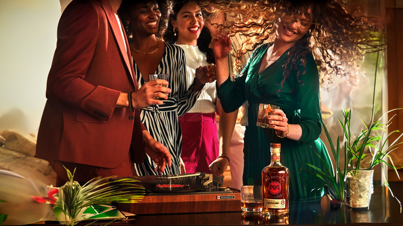 BACARDÍ Reserva Ocho rum bottle near a record player with people dancing and celebrating.