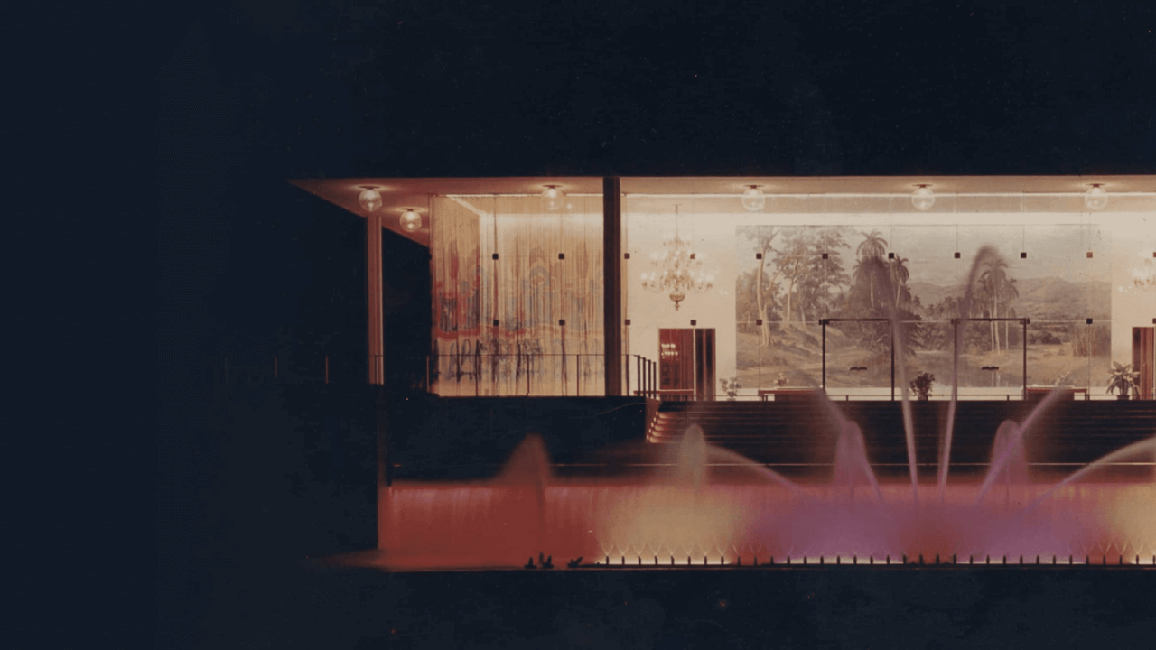 Mid-century modern building at night with illuminated fountains and warm-colored lighting.