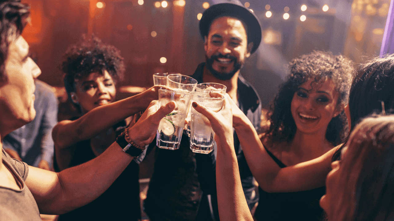 Group of people toasting with cocktails, surrounded by warm string lights.