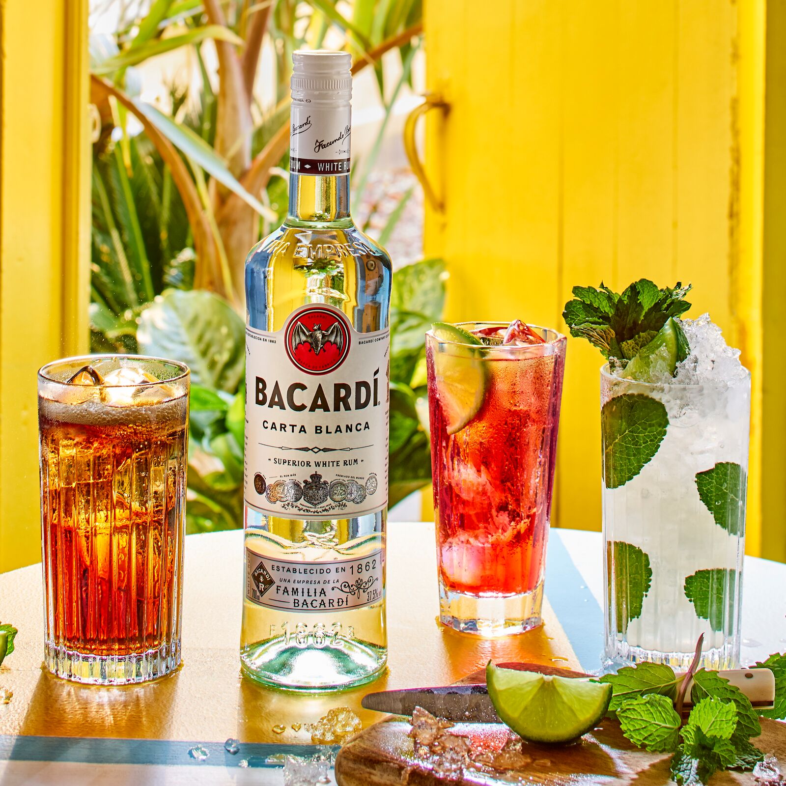 BACARDÍ Carta Blanca rum bottle with three different cocktails, lime wedges, and mint.
