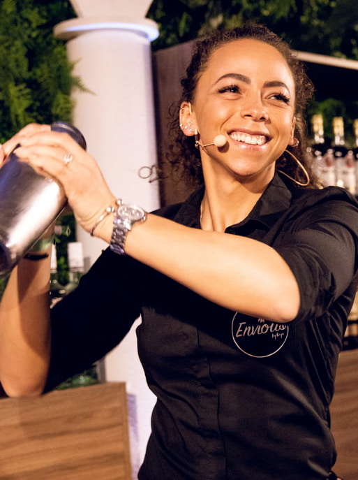 Bartender shaking a cocktail in a silver shaker while wearing a black collared shirt.