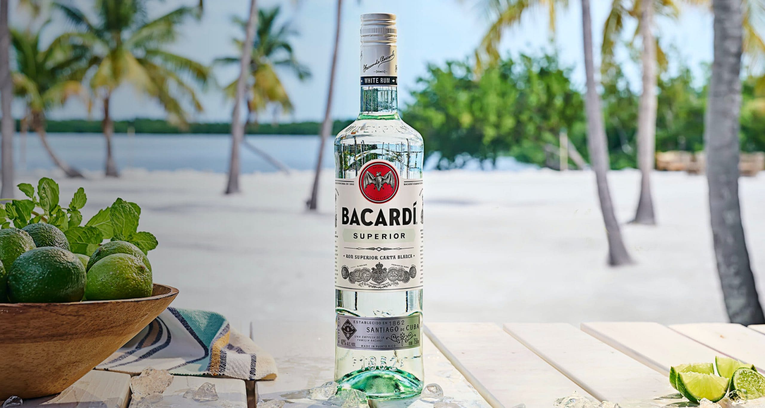 BACARDÍ Superior rum bottle with ice cubes, fresh limes, mint leaves in a wooden bowl.