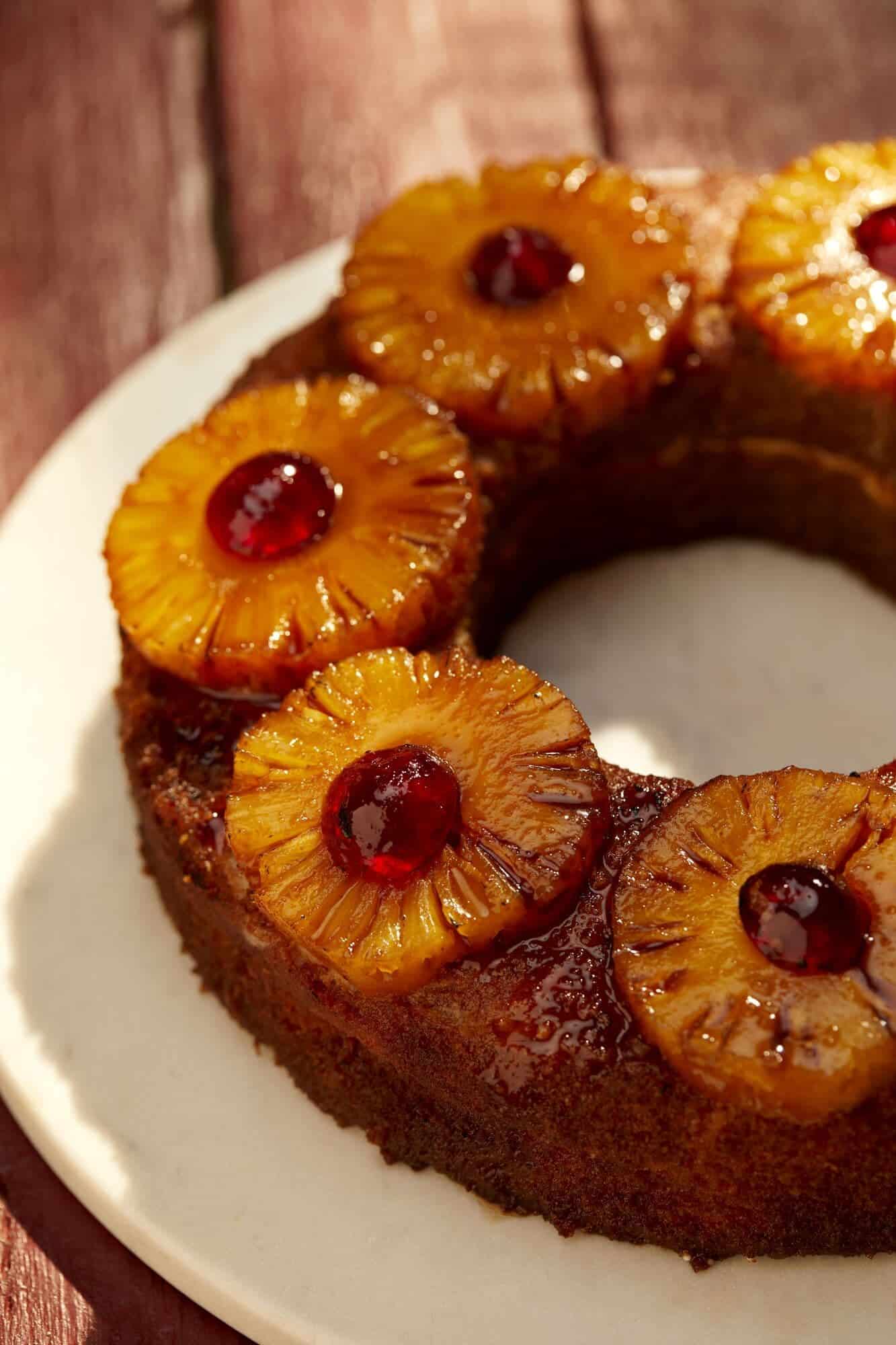 Close-up of golden-brown bundt cake with caramelized pineapple rings and bright red maraschino cherries.