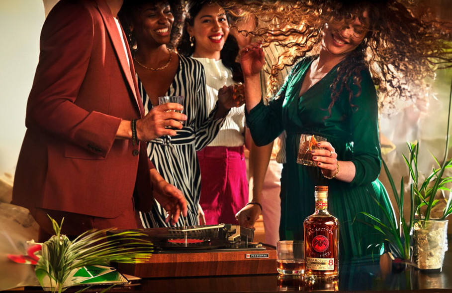 BACARDÍ Reserva Ocho rum bottle and glass at a house party with people celebrating.