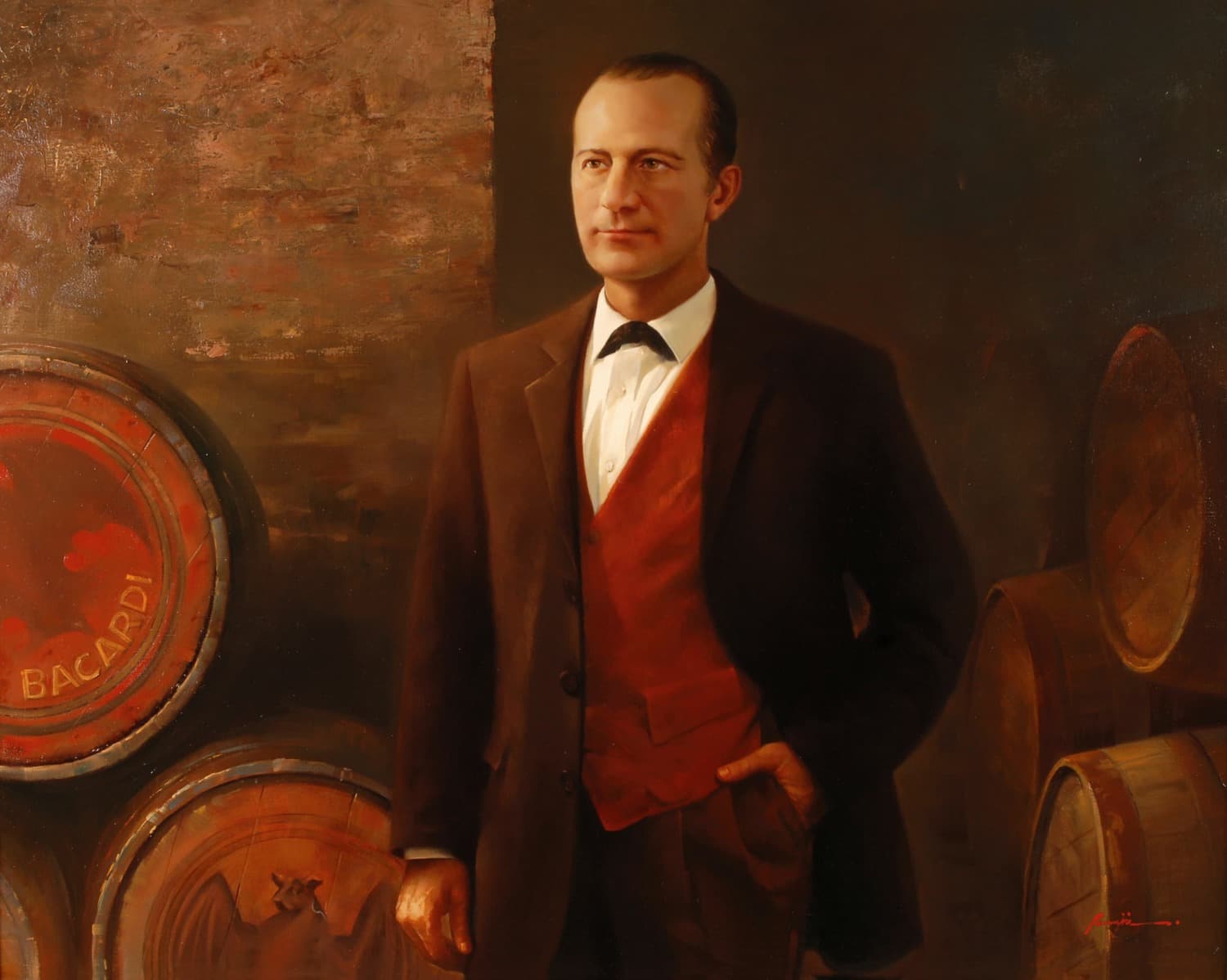 Portrait of a man in a dark suit, white shirt, red vest, standing near wooden barrels.