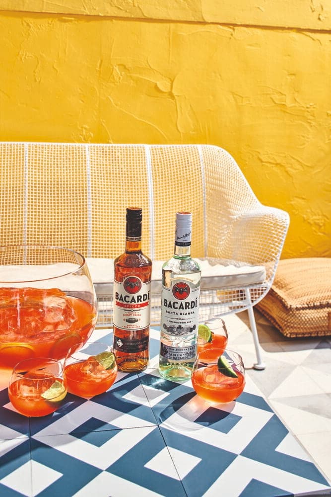 Two BACARDÍ rum bottles next to punch bowl and cocktail glasses with lime wedges.