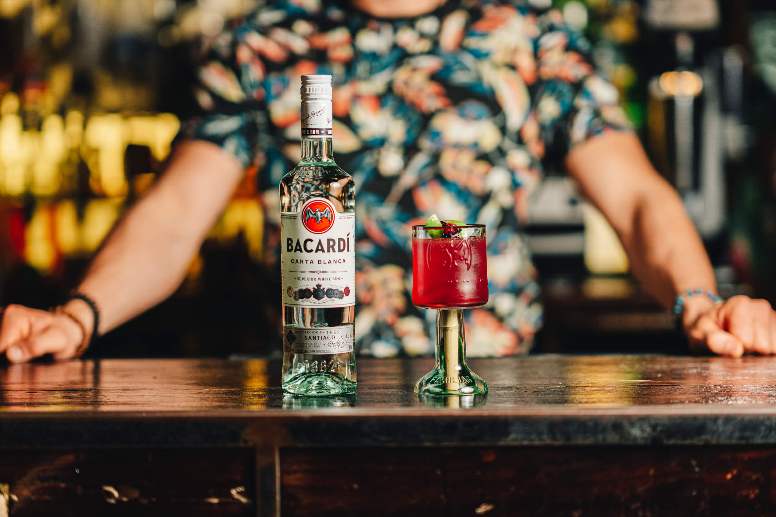 BACARDÍ Carta Blanca rum bottle beside a vibrant red cocktail in a green-stemmed glass.