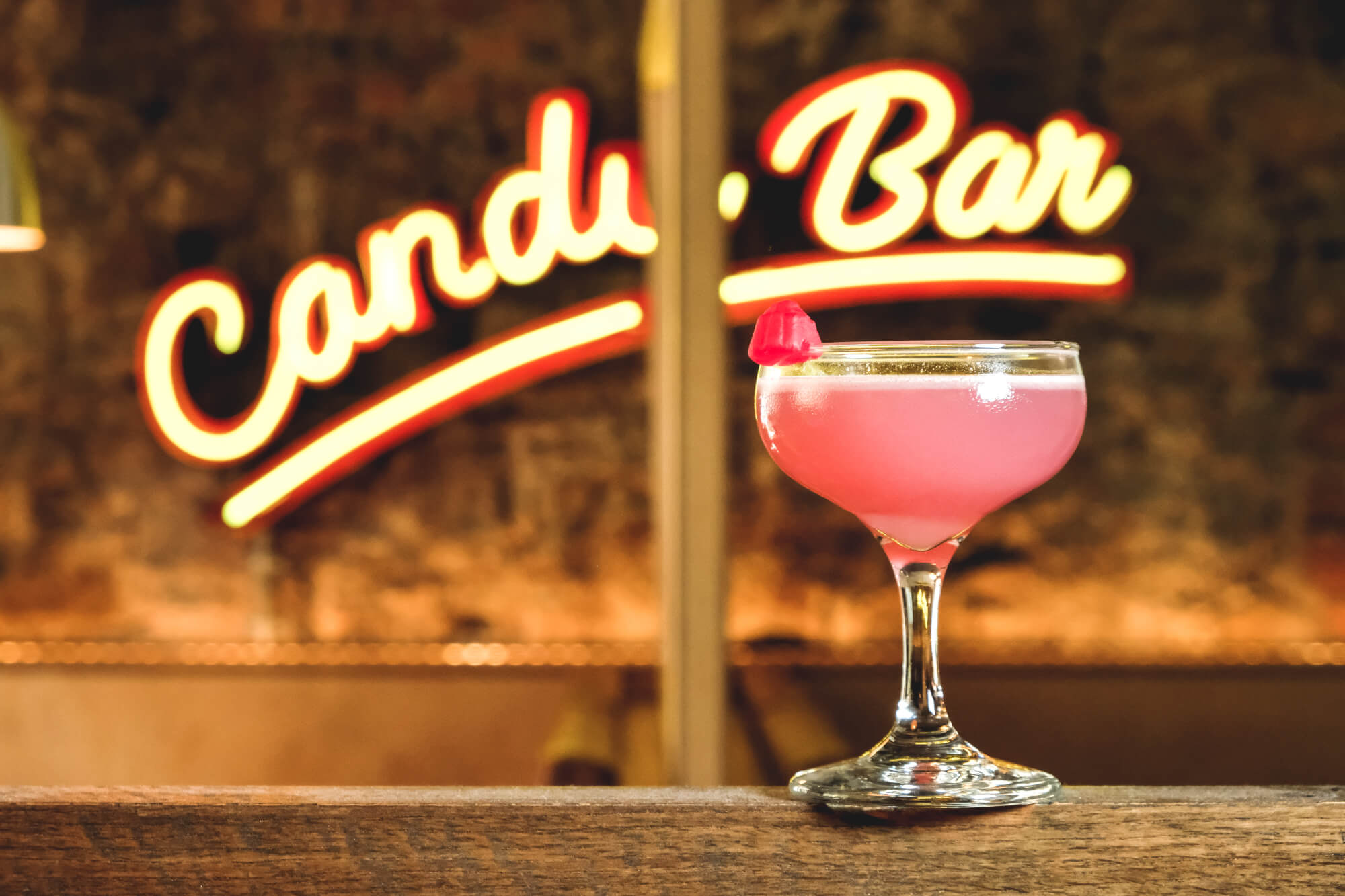 Pink cocktail in a coupe glass with a small red berry garnish.