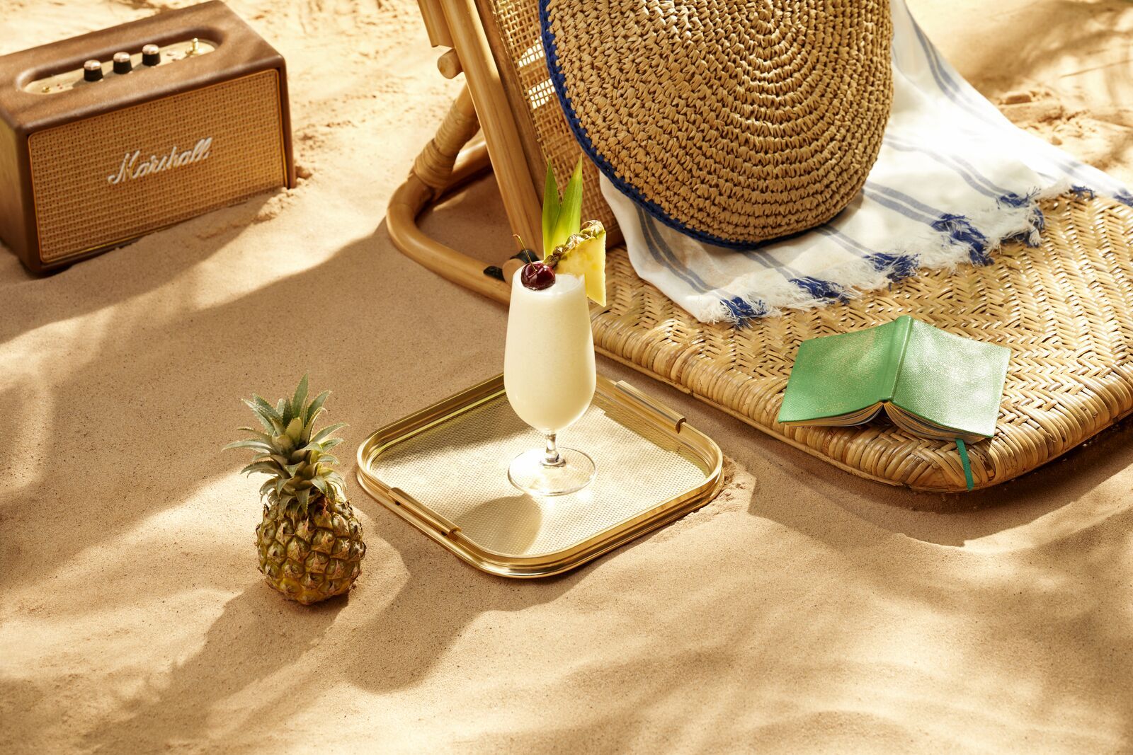Creamy white cocktail with cherry, pineapple wedge on a gold tray near a whole pineapple.