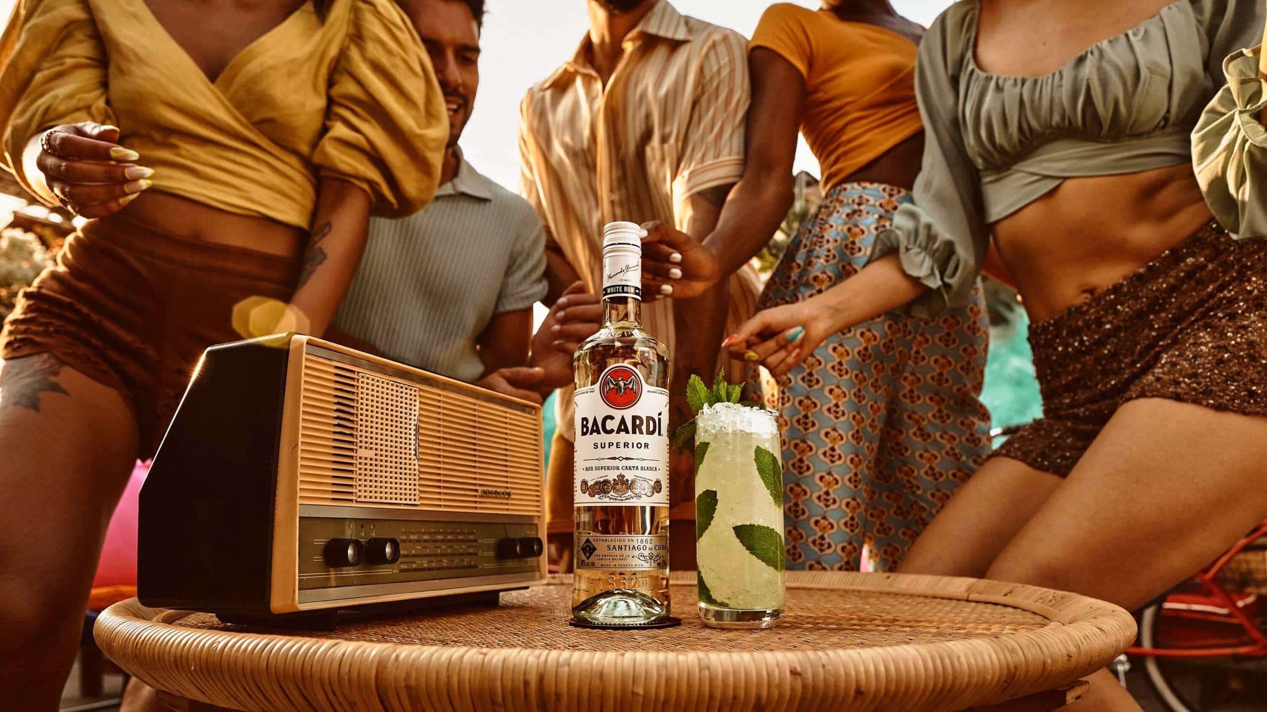BACARDÍ Superior rum bottle and mojito cocktail with vintage radio at a lively social gathering.