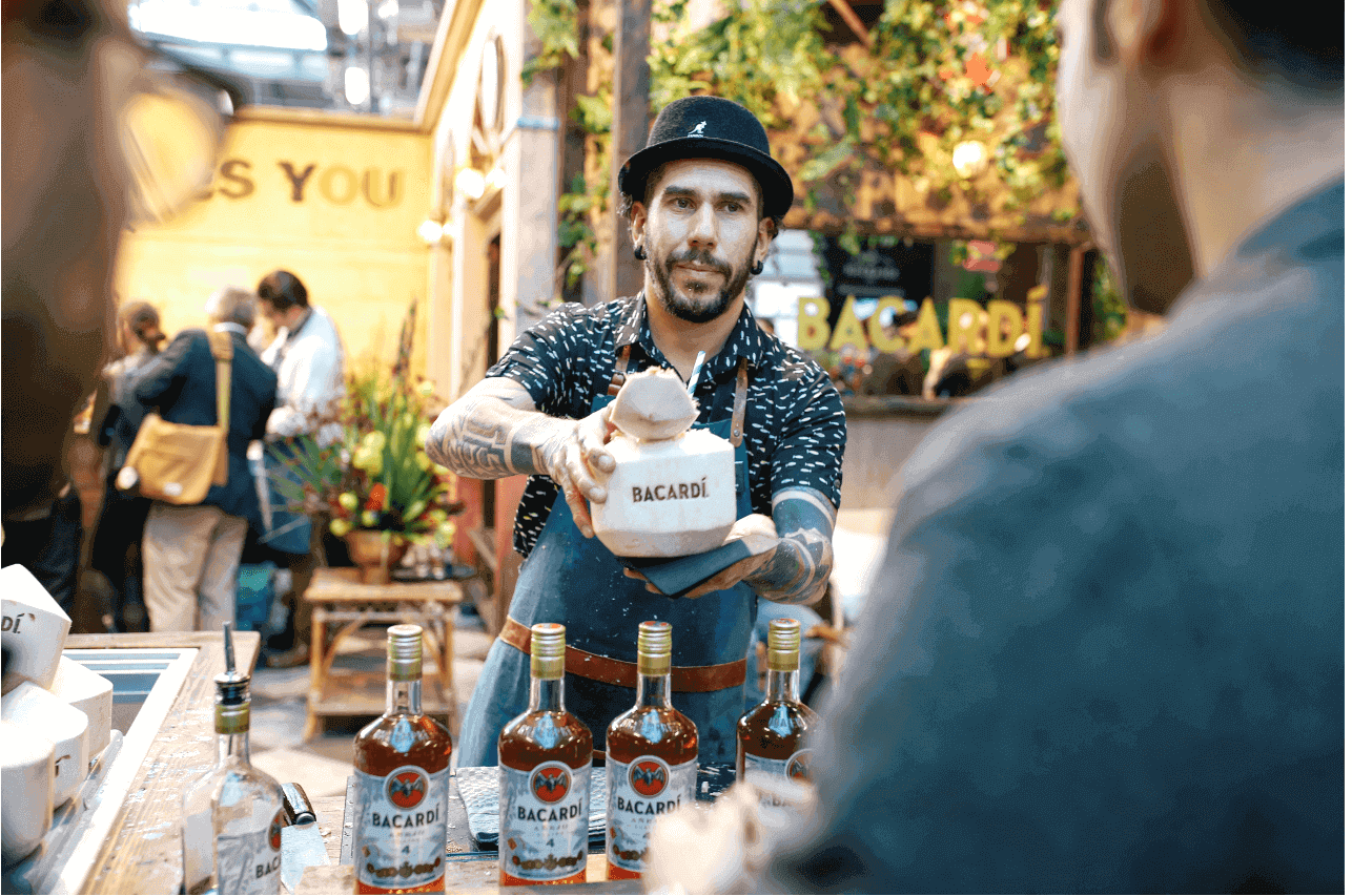Bartender presenting a coconut drink with BACARDÍ bottles lined up.