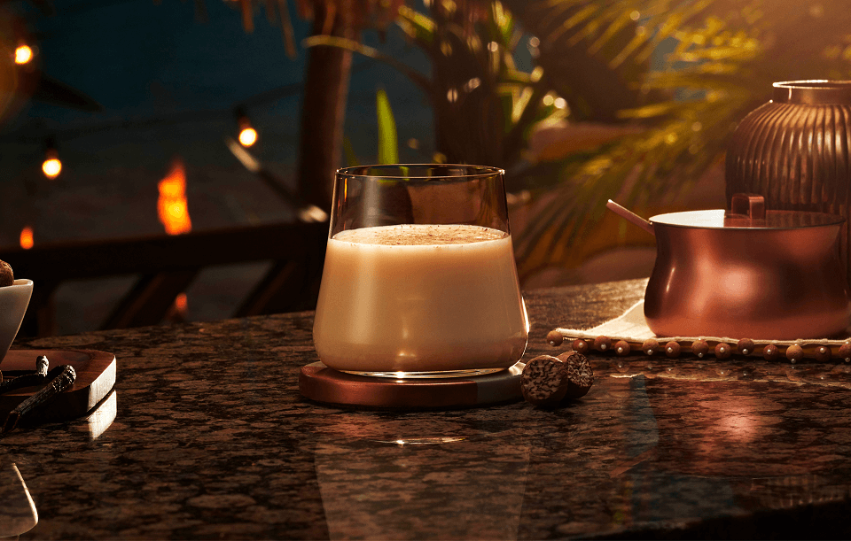 Creamy eggnog topped with grated nutmeg, served with whole nutmeg seeds and a copper pot.