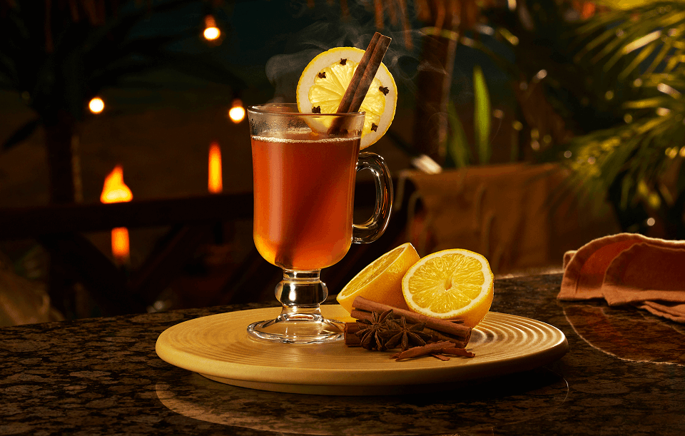 Hot buttered rum in a glass mug with lemon wheel, cloves, cinnamon stick, star anise.