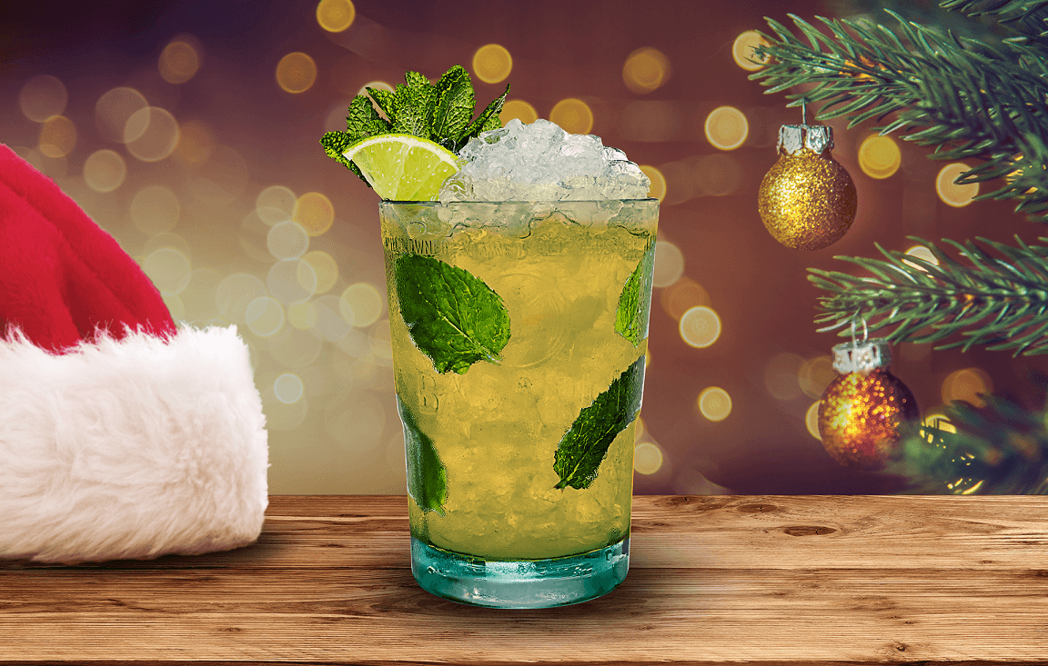 Mojito cocktail with crushed ice, mint leaves, lime wedge near a Santa hat and Christmas ornament.