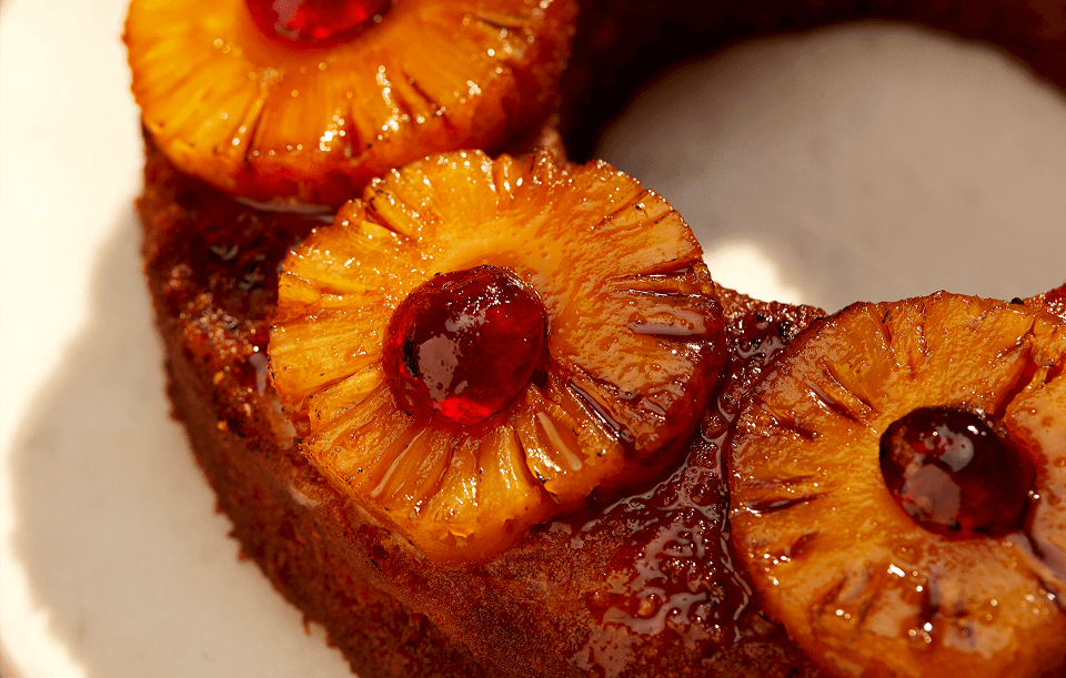 Close-up of pineapple upside-down cake with caramelized pineapple rings, bright red cherries.