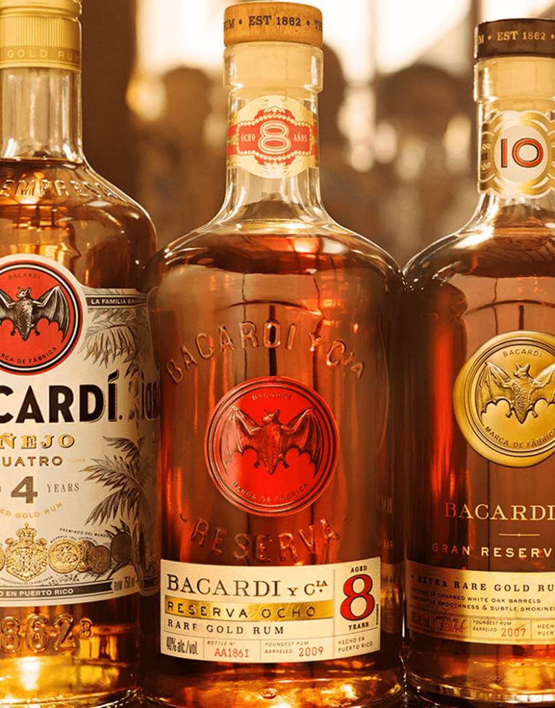 Three BACARDÍ rum bottles: Añejo Cuatro, Reserva Ocho, Gran Reserva Diez, showcasing amber liquids.