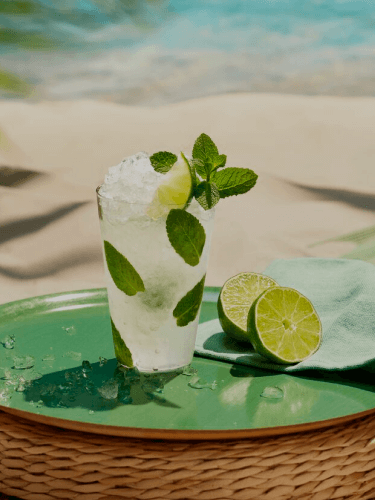 Mojito cocktail in tall glass with crushed ice, mint leaves, lime wedge on green tray.