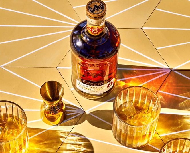 BACARDÍ Reserva Ocho rum bottle with two glasses, ice, and golden jigger.