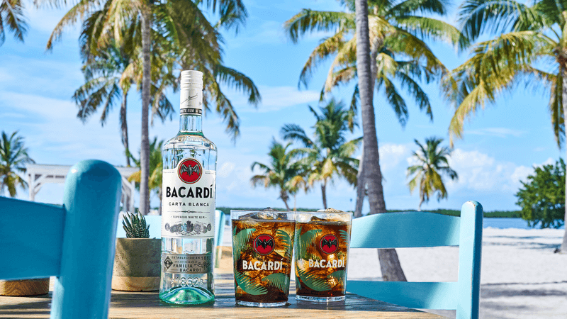 BACARDÍ Carta Blanca rum bottle with two rum and cola cocktail glasses.