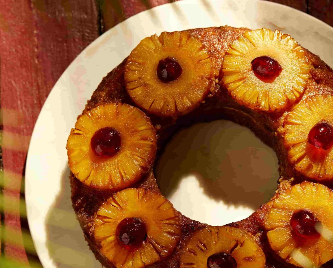 Ring-shaped pineapple upside-down cake topped with caramelized pineapple slices, maraschino cherries.