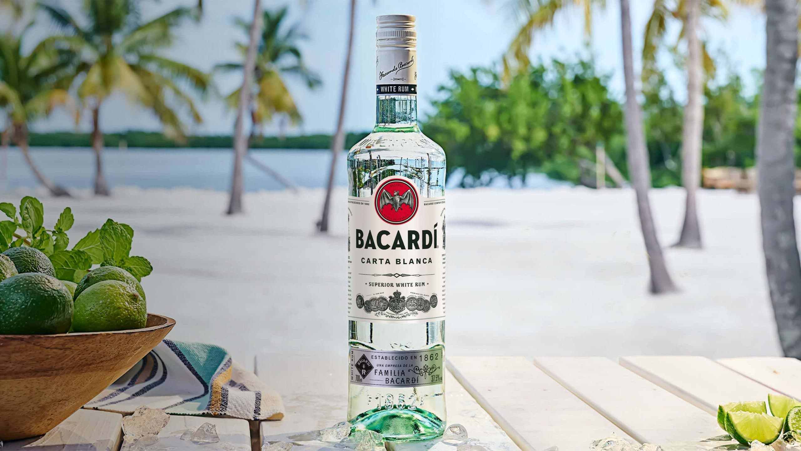 BACARDÍ Carta Blanca rum bottle with ice cubes, fresh limes, mint leaves scattered nearby.