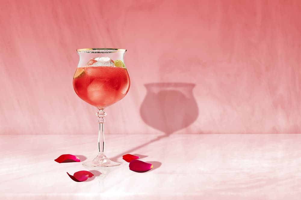 Pink raspberry spritz cocktail in gold-rimmed glass with ice, lime wedge, rose petals.