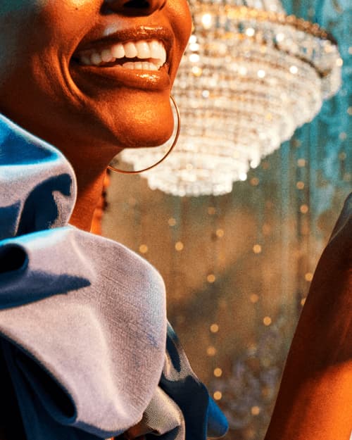 Close-up of a smile with gold hoop earring, blurred chandelier in background.