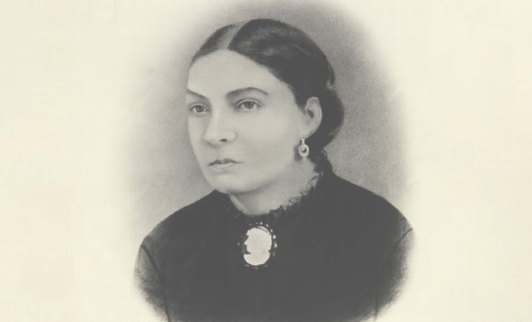 Woman in historical attire with cameo brooch and pearl earring, captured in soft black and white portrait.