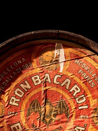 Close-up of vintage BACARDÍ barrel label with red, yellow colors, bat logo, historical text.