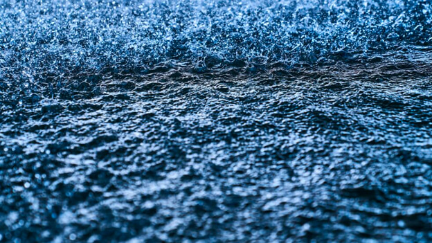 Close-up of raindrops creating ripples and splashes on a dark blue water surface.