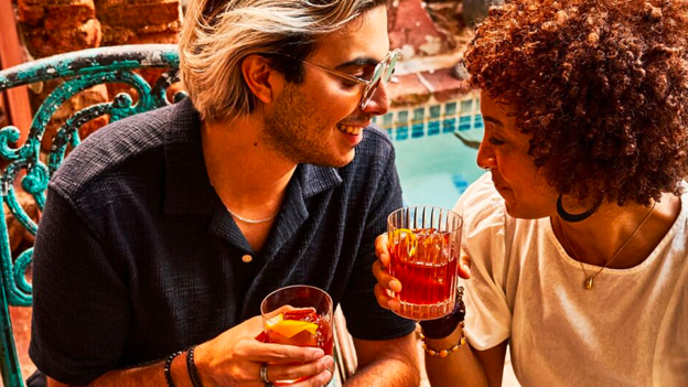 Two people sitting together, each holding a dark orange cocktail with citrus garnish.
