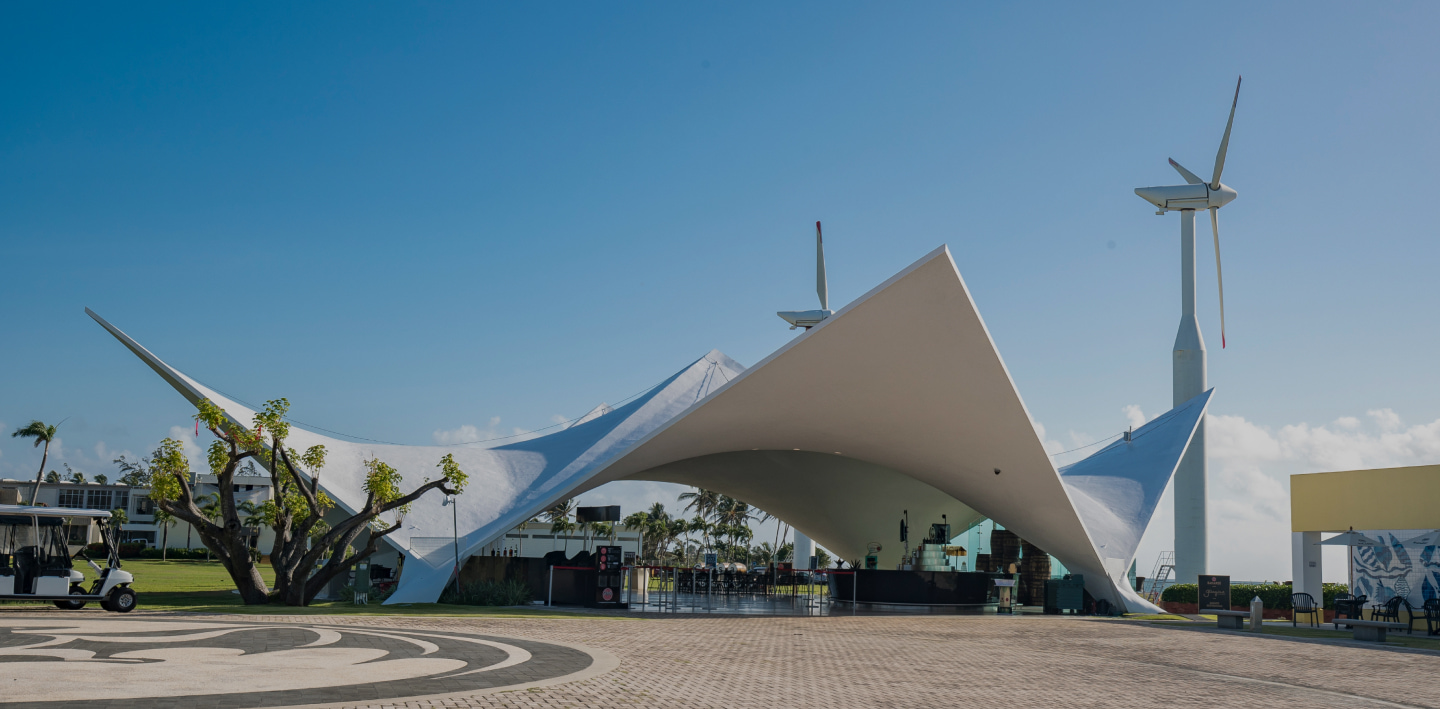 Modern white tensile structure with curved roof, featuring a tall white wind turbine nearby.