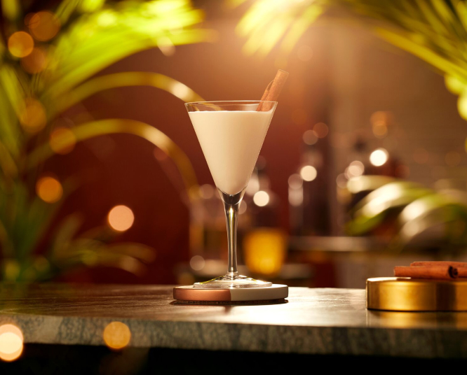 White cocktail in martini glass, garnished with cinnamon stick.