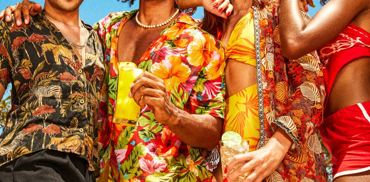 Four people standing together, holding bright yellow and light cocktails in tropical-patterned attire.