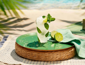 Mojito cocktail with lime and mint on green ceramic plate, placed on woven tray.