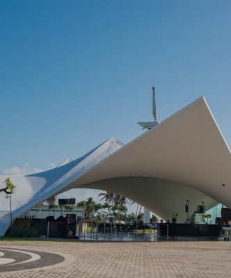 Large white modern tensile pavilion with curved roof under clear blue sky.